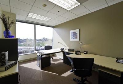 Private office featuring an L-shaped desk and large windows with greenery views.