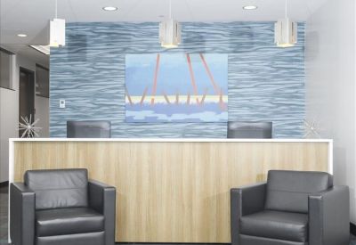 Reception area featuring a wood-fronted desk, grey leather armchairs, and blue textured wallpaper.