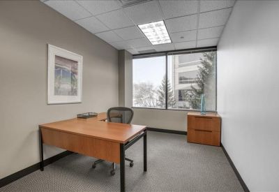Private office with a light wood desk, ergonomic chair, and large window.