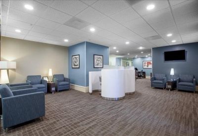 Lounge area with blue armchairs, white cylindrical privacy booths, and a TV.