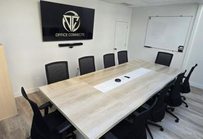 Conference room with large table and wall-mounted screen displaying logo.