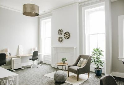 Bright office lounge with a grey armchair, fireplace, and woven wall art.