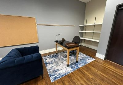 Corner office view with built-in white shelving, a desk on an area rug, and a dark wood door.
