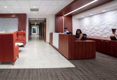 Modern reception area featuring a warm wood desk, textured white feature wall, and red lounge seating.