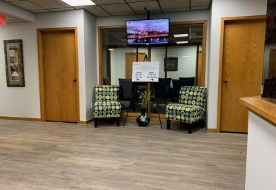 Bright reception waiting area with patterned armchairs and a wall-mounted TV.