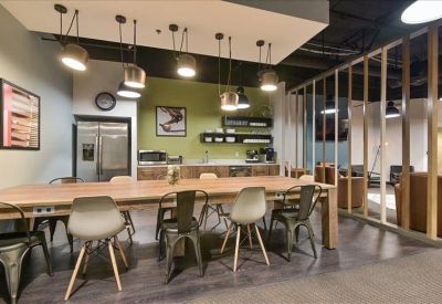 Communal breakroom with a large wooden table, industrial-style lighting, and a kitchen area.