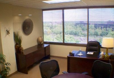 Executive office suite with a dark wood desk and a large window with city views.