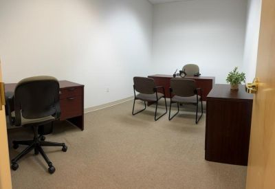 Small two-person internal office featuring wooden desks and a potted plant.