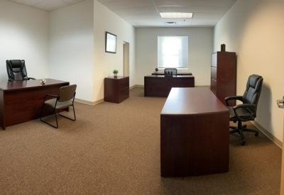 Spacious private office suite with multiple dark wood desks and black leather chairs.