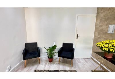 Cozy reception waiting area with two black armchairs and a green potted plant.