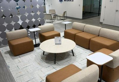 Bright communal lounge with brown modular seating, small white side tables, and a grey circle-patterned divider.