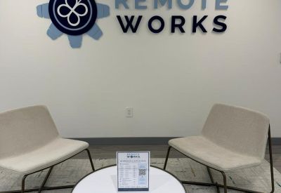 Reception area featuring wall-mounted company branding above two modern cream chairs and a round coffee table.