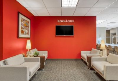Business lounge with comfortable white sofas and a wall-mounted TV on a red wall.