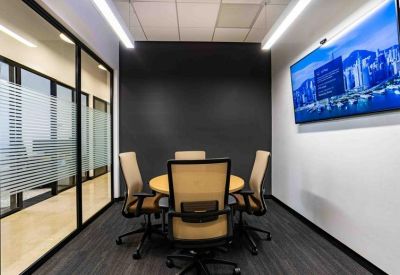 Four-person meeting room with a round table and a wall-mounted monitor.