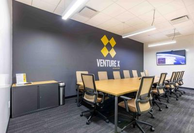 Large conference room with a wooden table, Venture X branding on a dark wall, and a large TV.