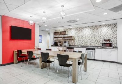 Bright office kitchen and breakroom with a red feature wall, long dining table, and modern appliances.