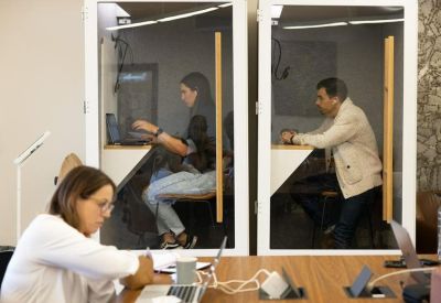Close-up of glass-walled private phone booths with individuals working on laptops.