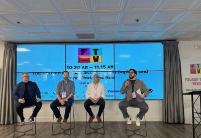 Panel discussion with four speakers seated on stools in front of a large digital display screen.