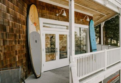 Exterior entrance of a shingle-sided building with white railings and decorative surfboards.