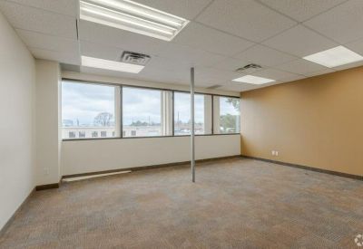 Empty carpeted office with neutral walls and a wide window.