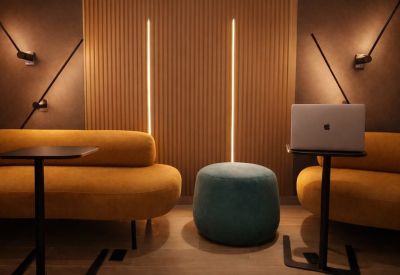 Lounge area with yellow sofas, a teal ottoman, and warm vertical light strips.