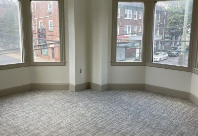 Spacious corner office with grey patterned carpet and two large bay windows.