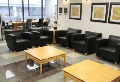 Modern lounge area featuring black leather armchairs and light wood coffee tables.