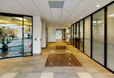 Brightly lit building corridor with glass partitions and polished tile flooring.