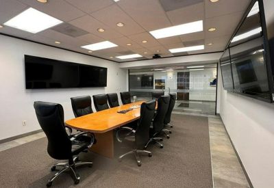 Professional conference room with a long wooden table, black ergonomic chairs, and wall-mounted screens.