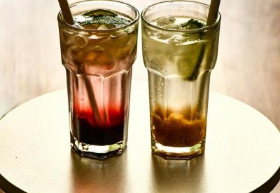 Two refreshing iced drinks with bamboo straws served on a small wooden stool.