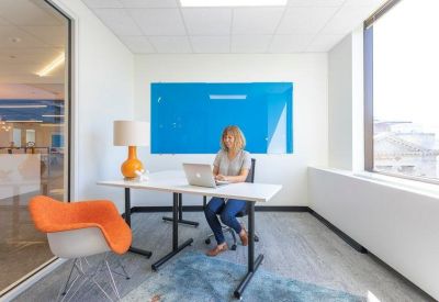 Private office suite with an orange accent chair and a bright blue whiteboard.