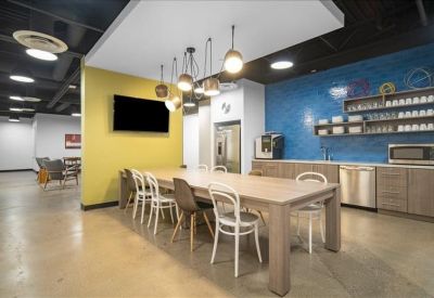 Modern communal kitchen and dining area with a yellow accent wall and blue backsplash.