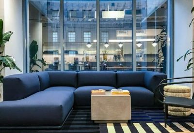 Lounge area featuring a large blue sectional sofa and potted plants in front of a glass wall.