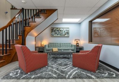 Cozy lounge area under a staircase with patterned rug and red armchairs.