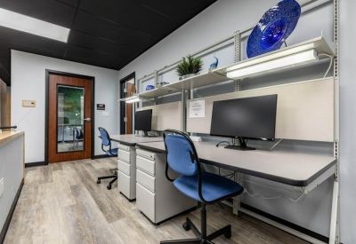 Modern workstation row with blue office chairs and dual monitors.