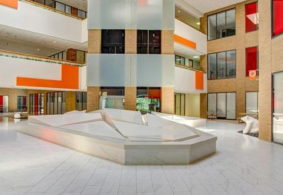 Spacious multi-level atrium lobby with white marble floors and vibrant orange accent walls.