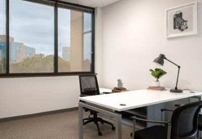 Sunlit office space with a minimalist white desk and a view of the surrounding greenery.
