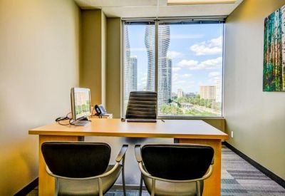 Private office suite with a wooden desk, two guest chairs, and a window overlooking high-rise buildings.