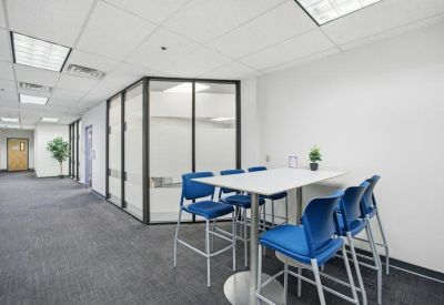 Modern breakout area with a high-top white table, blue bar stools, and glass partitions.