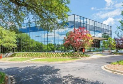 Polished glass office building reflecting the surrounding trees and blue sky.