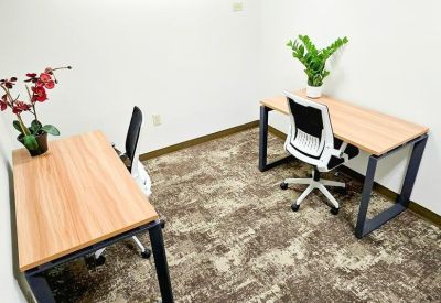 Two-person private office with light wood desks and patterned brown carpet.