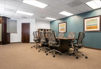 Professional boardroom with a large dark wood table, mesh chairs, and framed wall art.