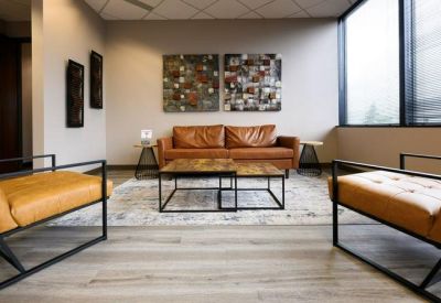 Reception waiting area with a tan leather sofa, matching armchairs, and a large window.