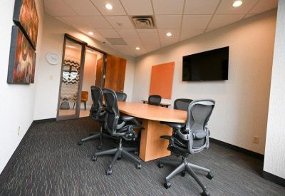 Six-person meeting room with an oval wooden table, black mesh chairs, and a wall-mounted TV.