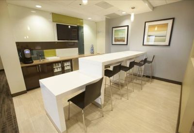 Sleek communal kitchen and break area with white countertops and bar seating.