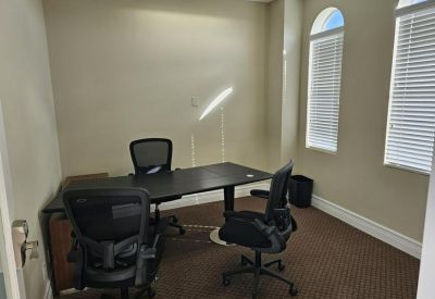 Private office suite with a dark wood desk, three mesh chairs, and arched windows.