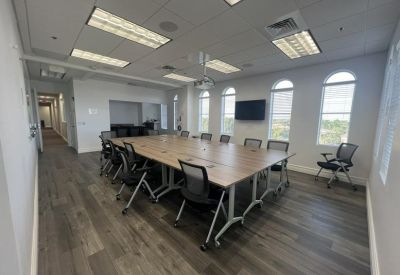 Spacious conference room with modular wooden tables, mesh chairs, and large arched windows.