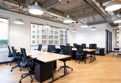 Open-plan office with wooden floors, rows of desks, and black ergonomic chairs.