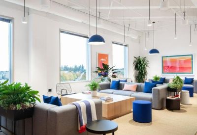 Bright breakout space with blue pendant lights, grey sofas, and vibrant wall art.