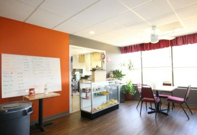 Bright breakroom with an orange accent wall, dining tables, and a snack display case.